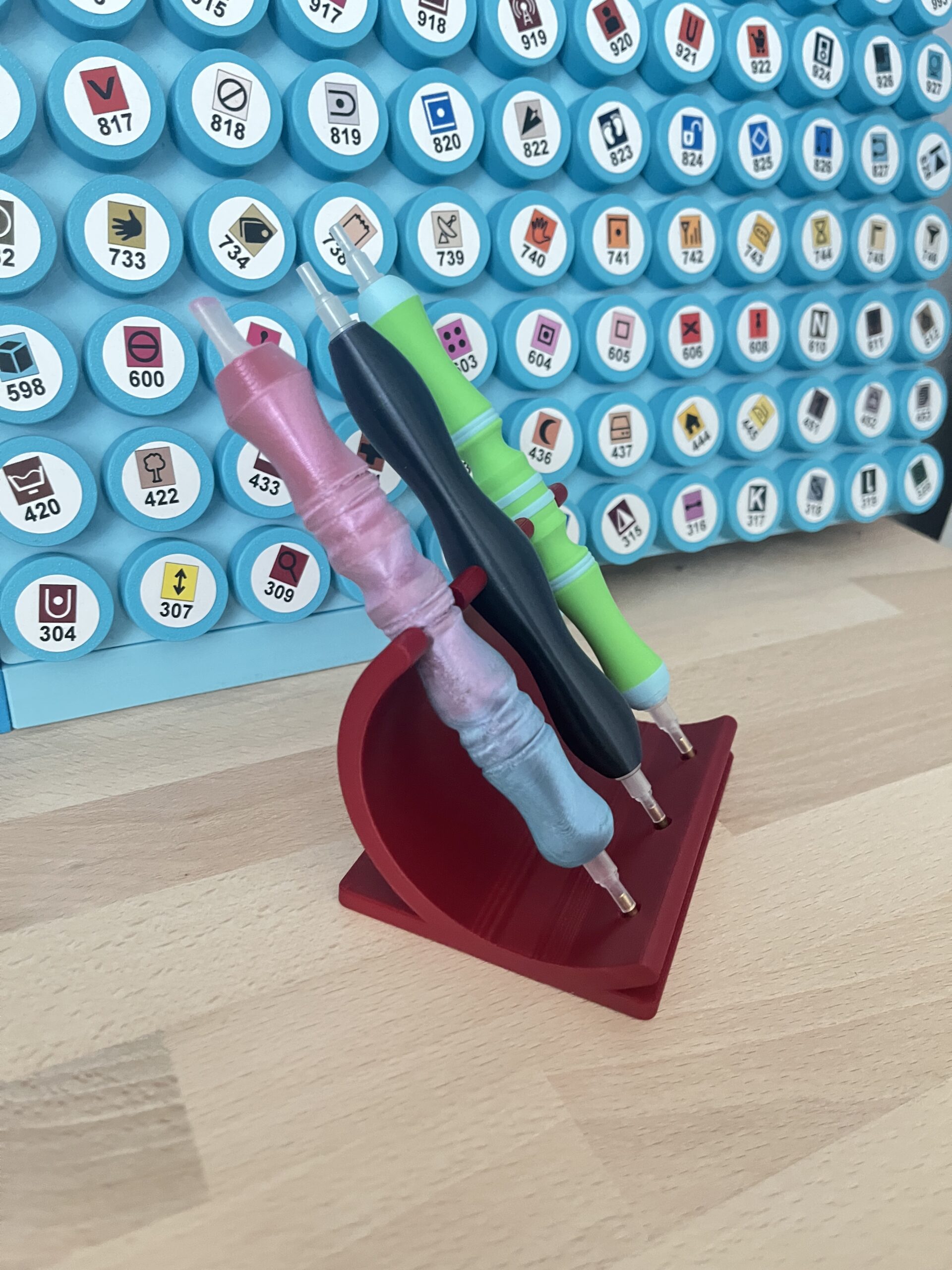 Seitliche Ansicht des roten, gebogenen Stifthalters mit drei schräg abgelegten Diamond-Painting-Stiften.